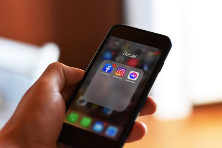 Mano sosteniendo un smartphone mostrando aplicaciones de redes sociales en pantalla
