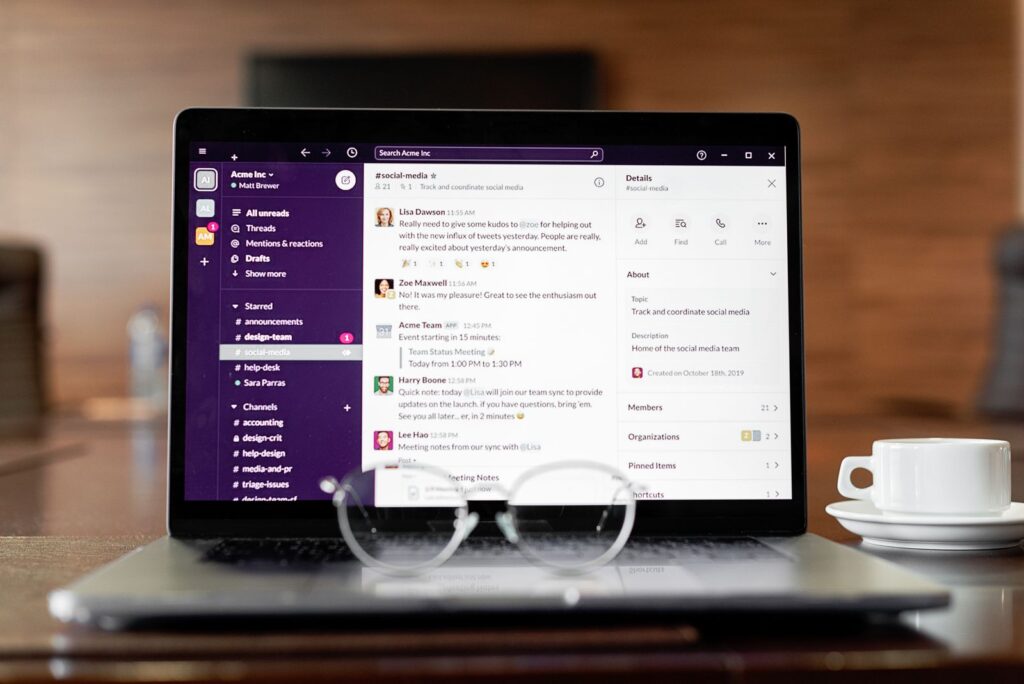 Laptop mostrando una aplicacion de mensajeria, con lentes y una taza de cafe sobre una mesa de madera