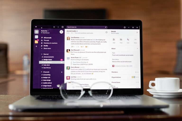Laptop mostrando una aplicacion de mensajeria, con lentes y una taza de cafe sobre una mesa de madera