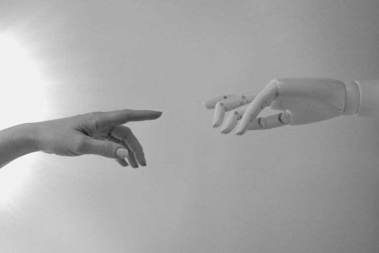 Fotografia en blanco y negro de una mano humana y una mano robotica acercandose