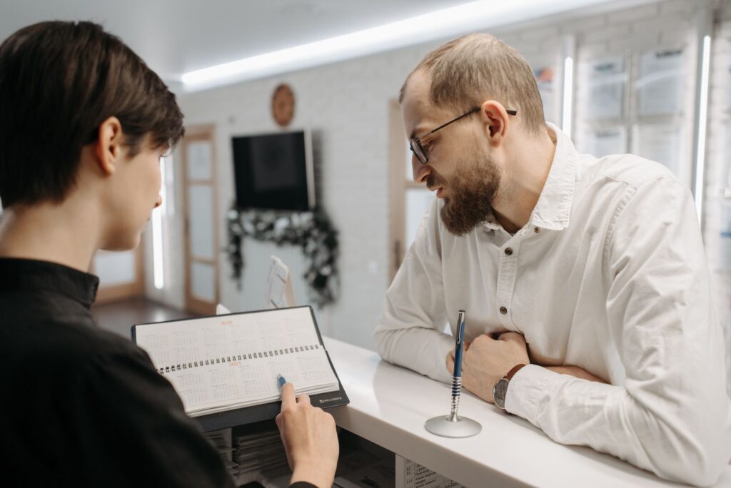 Recepcionista mostrando un calendario a un cliente en el mostrador de una clinica